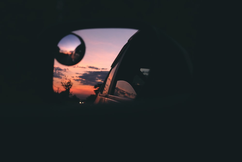 un espejo retrovisor con una puesta de sol en el fondo