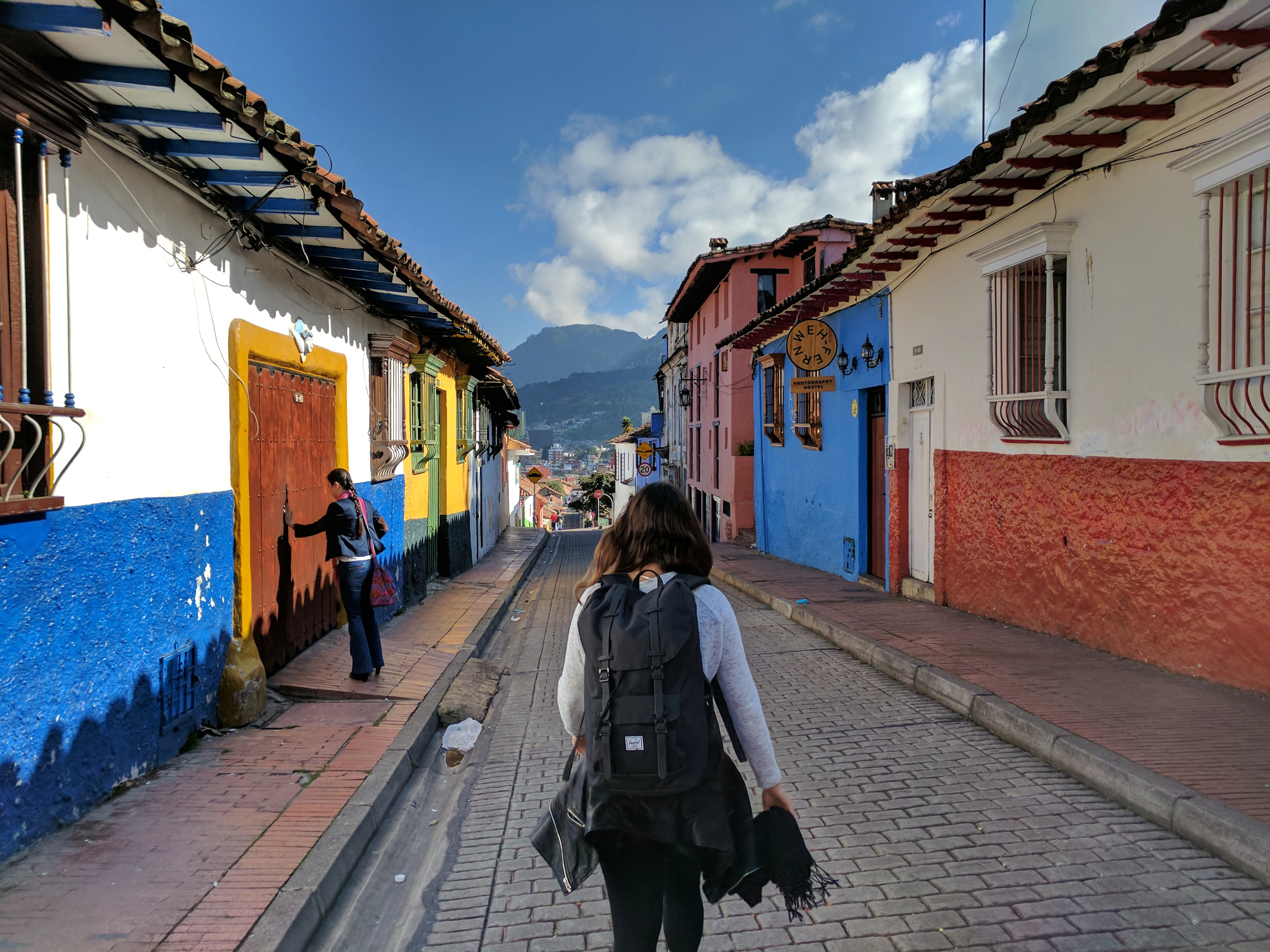 A traveller with a backpack walks a cobbled street of colourful colonial houses in La Candelaria, Bogotá