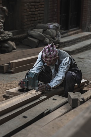 man in white striped shirt sitting on brown pallet holding gray power tool