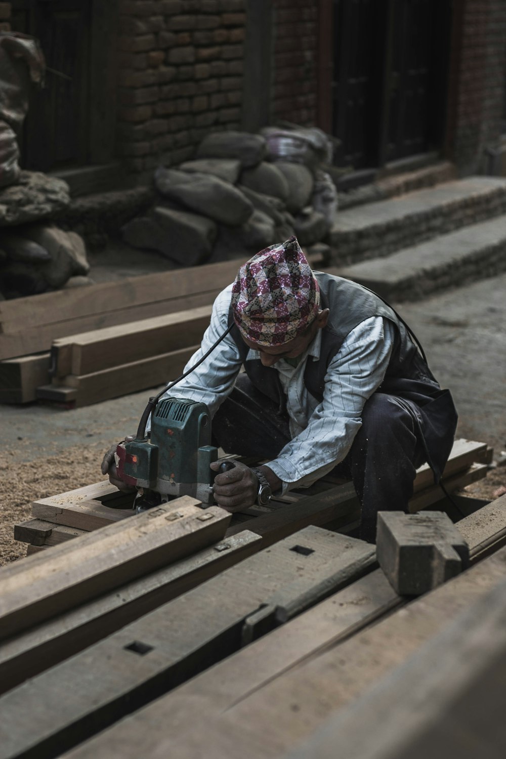 man in white striped shirt sitting on brown pallet holding gray power tool