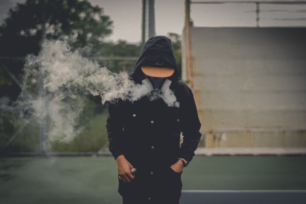 person wearing hooded jacket and respirator mask standing on green ground