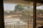 A view through a window screen showing an outdoor scene with blurred trees and landscape. The mesh of the screen creates a grid-like pattern, with the light filtering through it.
