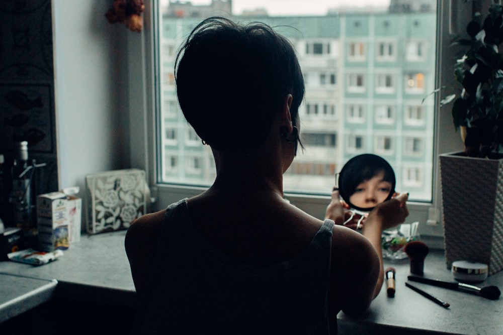 woman looking at mirror beside window