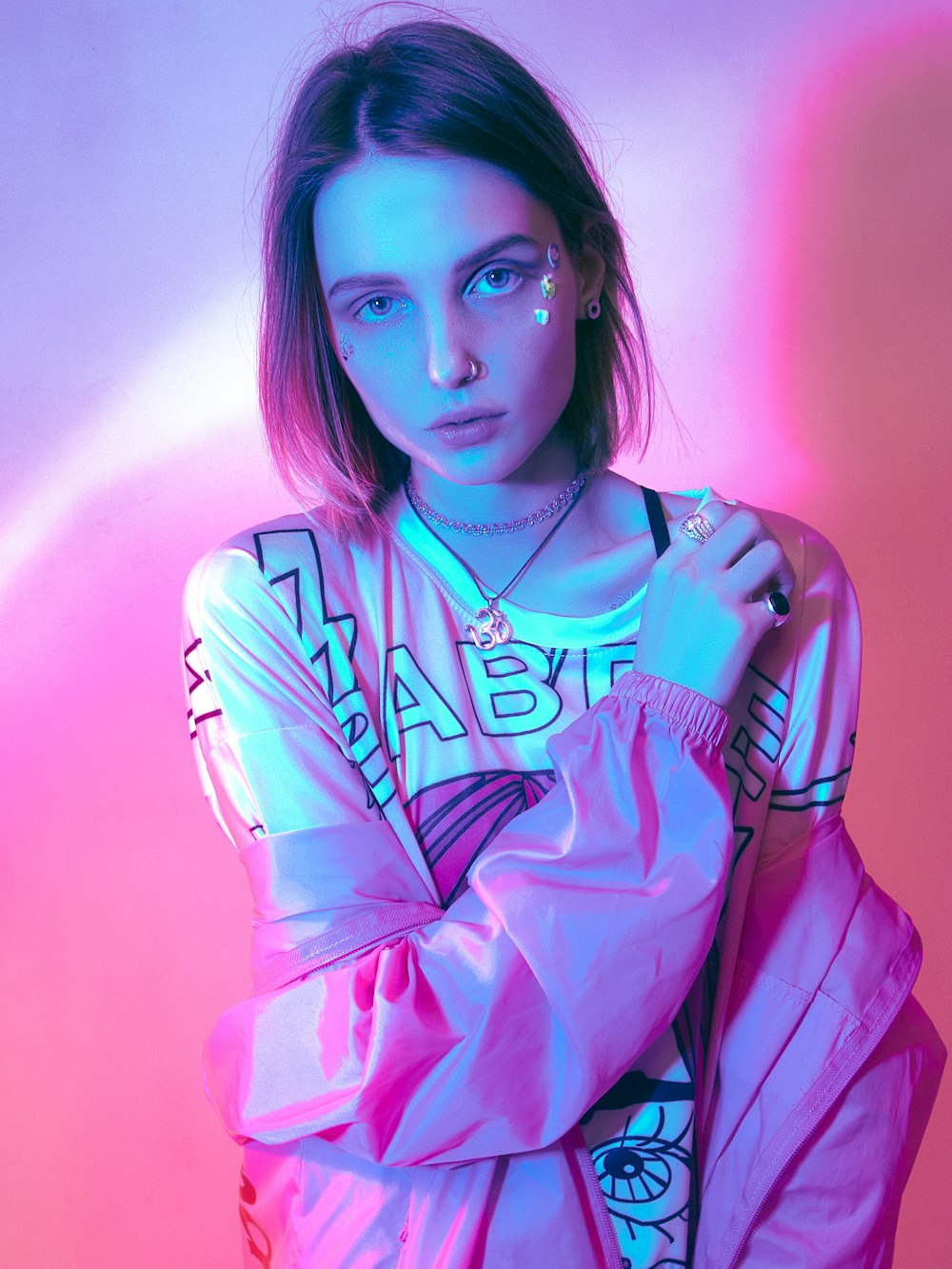 woman in white and pink shirt near white wall with necklace