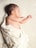 A newborn baby is peacefully sleeping on a soft, textured blanket. The baby is wrapped in a light-colored blanket with thin stripes, leaving one arm exposed. The infant's skin tone is warm and smooth, and their hair is dark.