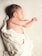 A newborn baby is peacefully sleeping on a soft, textured blanket. The baby is wrapped in a light-colored blanket with thin stripes, leaving one arm exposed. The infant's skin tone is warm and smooth, and their hair is dark.