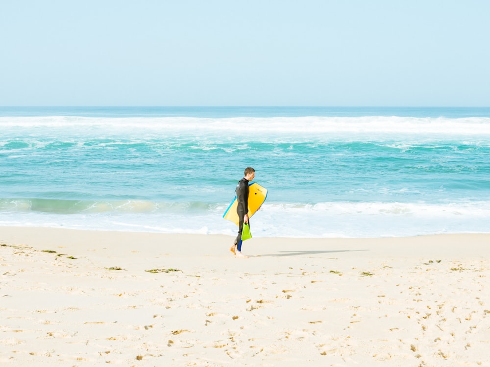 man walking on seashore holding yellow surfboard