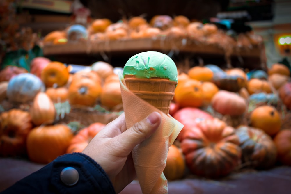 person holding ice cream in cone in front of pumpkins
