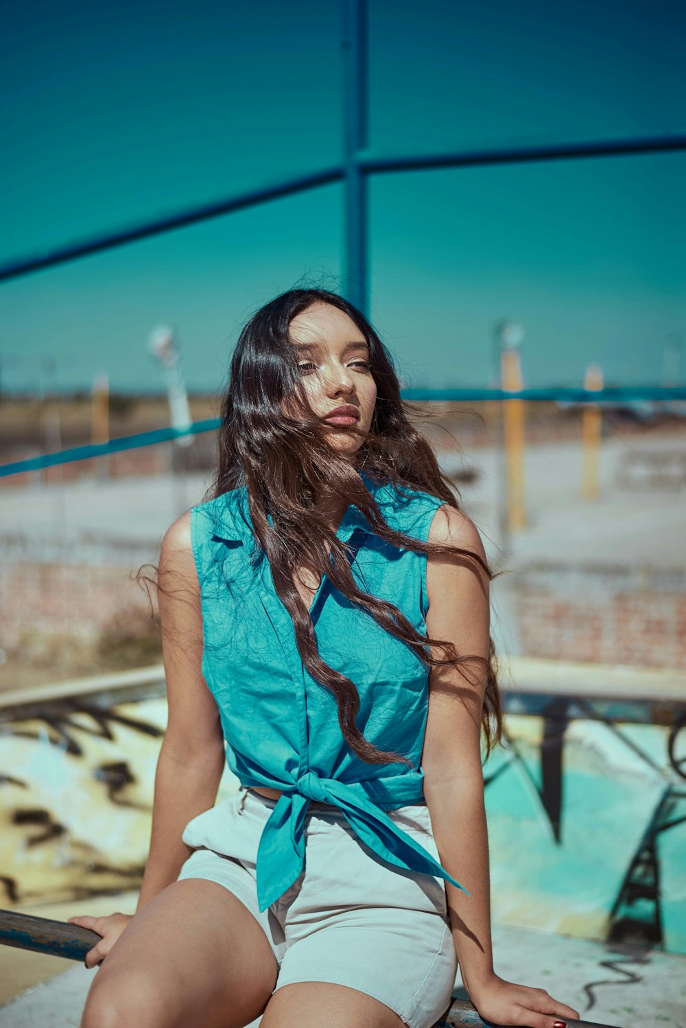 Donna in camicia verde acqua con nodo frontale seduta sull'asta di metallo grigia