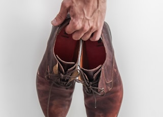 person holding pair of brown leather shoes