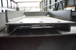 Close-up of a steelworker inspecting massive H-beams on a large-scale industrial site with amber lighting