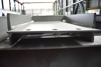 Close-up of a steelworker inspecting massive H-beams on a large-scale industrial site with amber lighting