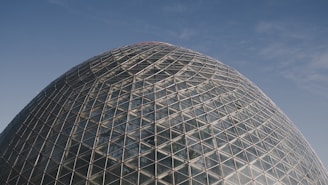 A vast transparent dome covering a green agricultural field under a clear blue sky.