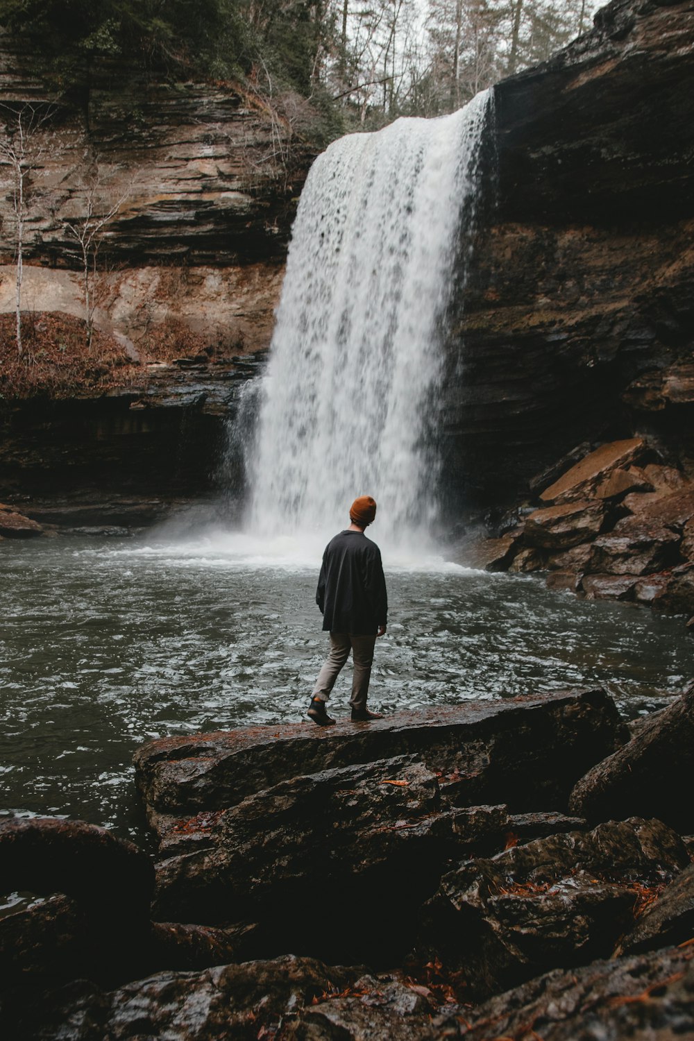 man standing on stone facing waterfalls