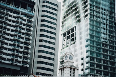 An urban landscape featuring modern high-rise buildings with glass facades, alongside an ornate clock tower. The architecture blends contemporary and classical elements, highlighting the contrast between sleek, reflective surfaces and intricate, historical design.
