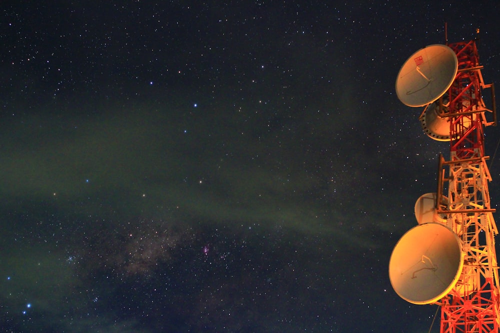 astrophotography red and white tower with satellites under milky way