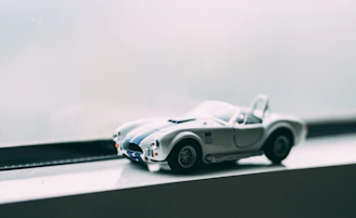 Miniature sports car model displayed on a wooden shelf with soft lighting