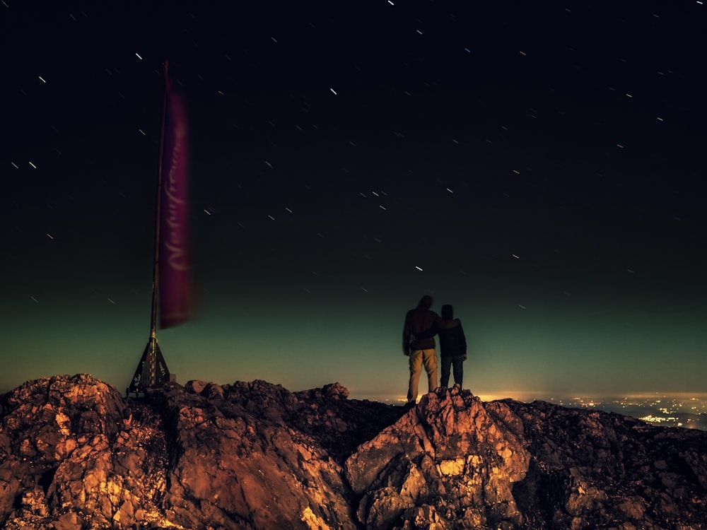 silhouette of two people standing on brown rocks under starry night