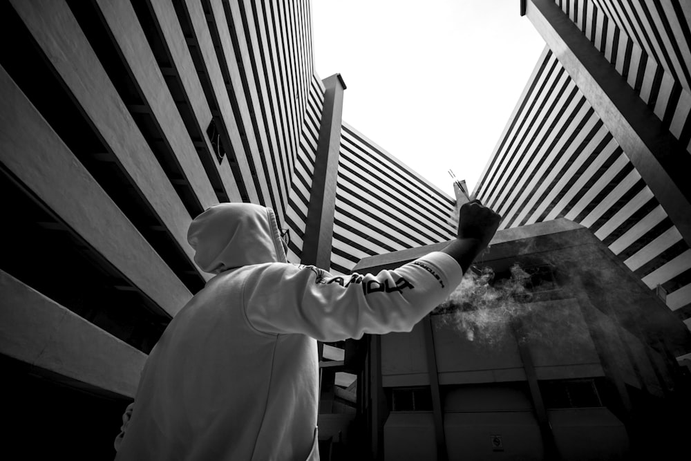 Foto en escala de grises de un hombre levantando la mano frente a un edificio