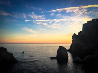 Sunset view over tranquil turquoise waters with a small boat gently drifting near rugged cliffs.