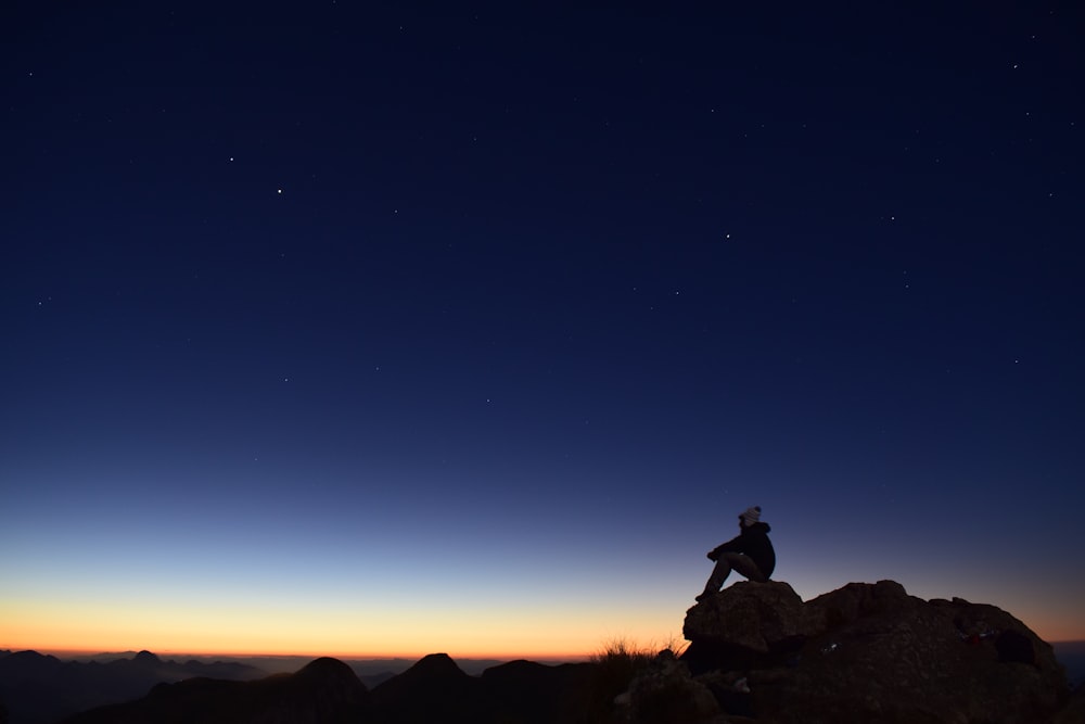 silhouette di persona seduta sulla roccia durante la notte