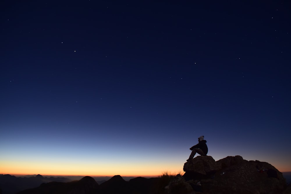 silhouette of person sitting on rock during night time