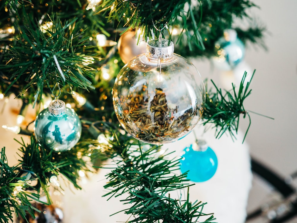 Kugeln aus klarem und blaugrünem Glas hängen am beleuchteten Weihnachtsbaum