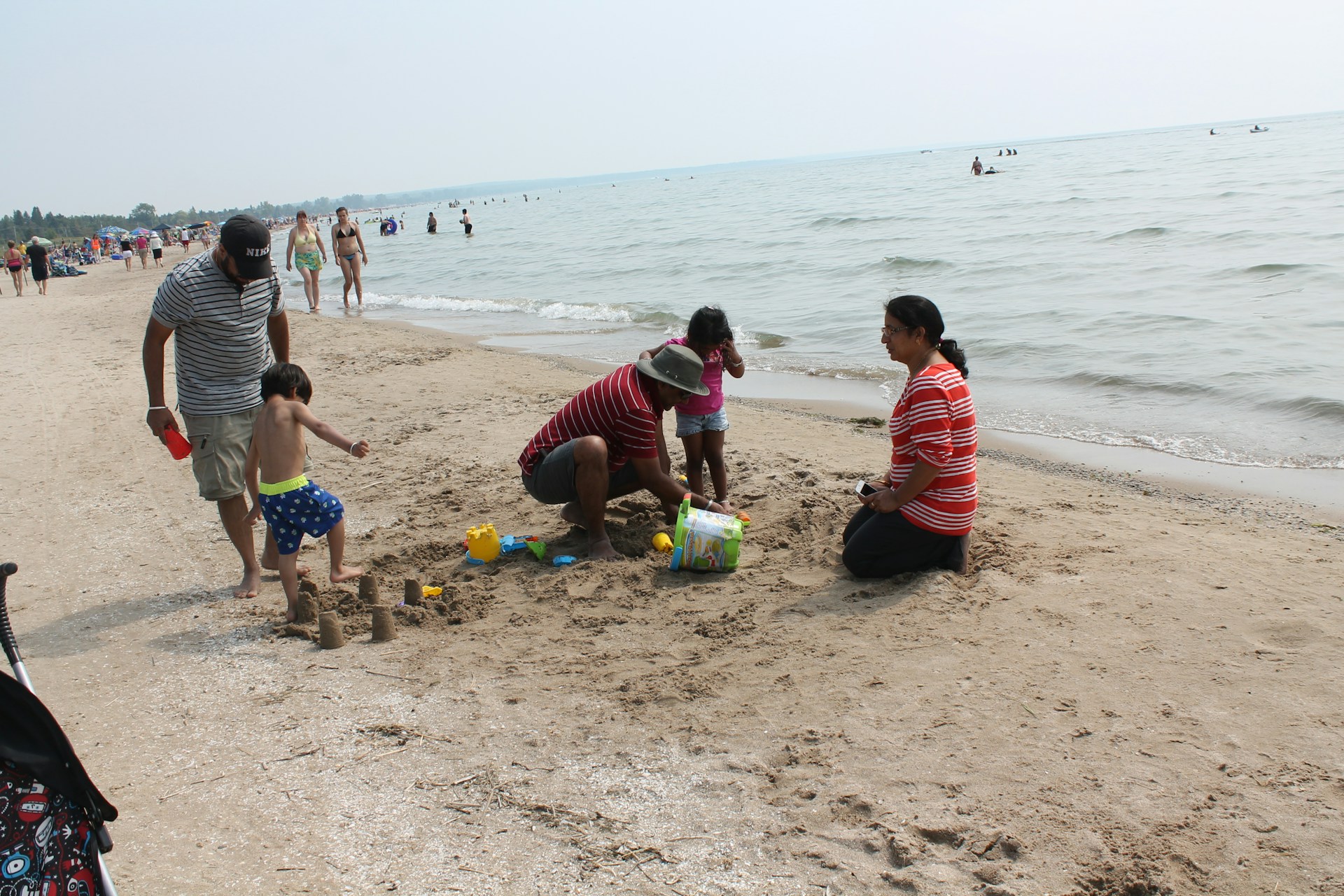 A family building sandcastles and playing near the gentle waves on a sunny beach with colorful umbrellas.