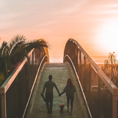 man and woman holding hand while walking on bridge