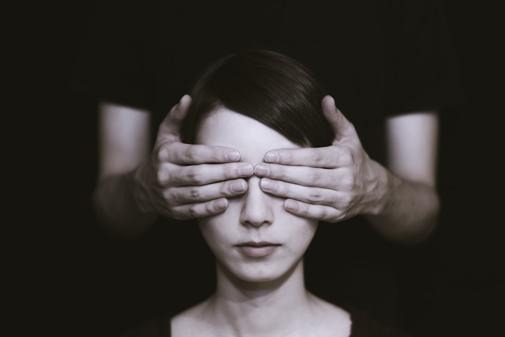 person covering the eyes of woman on dark room