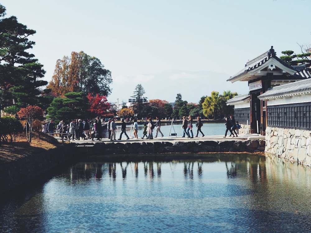 people walking on concrete bridge with body of water under gray sky during daytime