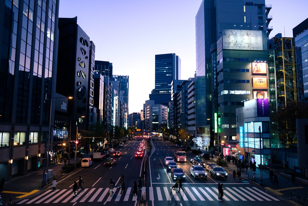 people crossing the street with vehicles between high rise buildings