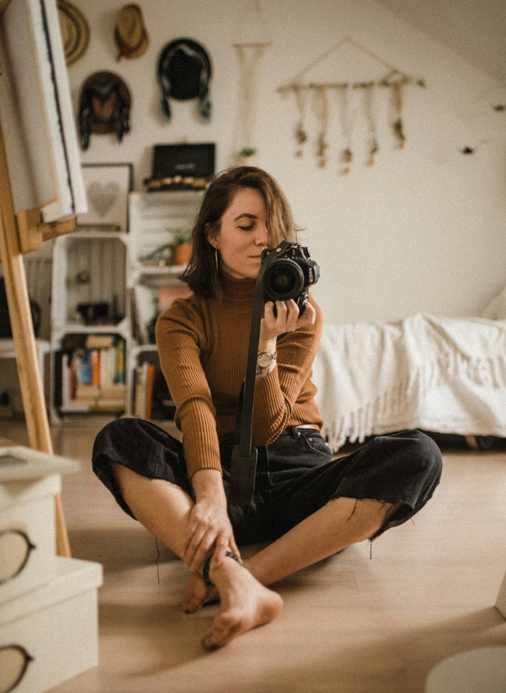 茶色の木製の床に座り、部屋で黒いデジタル一眼レフカメラを持っている女性