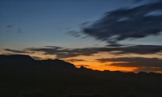 A cinematic wide-angle shot of a sunset over a mountain range, emphasizing natural colors and shadows.