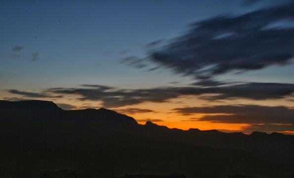 A cinematic wide-angle shot of a sunset over a mountain range, emphasizing natural colors and shadows.