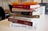 A stack of business and entrepreneurship books on a table. The titles are oriented towards strategies, innovation, and startup guidance, including 'Zero to One', 'Ego is the Enemy', and 'The Startup Owner's Manual'. The setting appears to be in a modern office or study environment.
