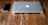 A closed, silver laptop with an apple logo next to a black smartphone on a rustic wooden table.