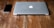 A closed, silver laptop with an apple logo next to a black smartphone on a rustic wooden table.