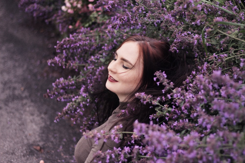 woman wearing gray top taking photo beside purple flowers at daytime