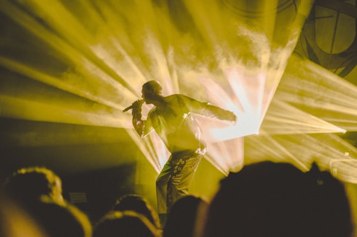 Artist performing live on stage with vibrant yellow and black lighting.