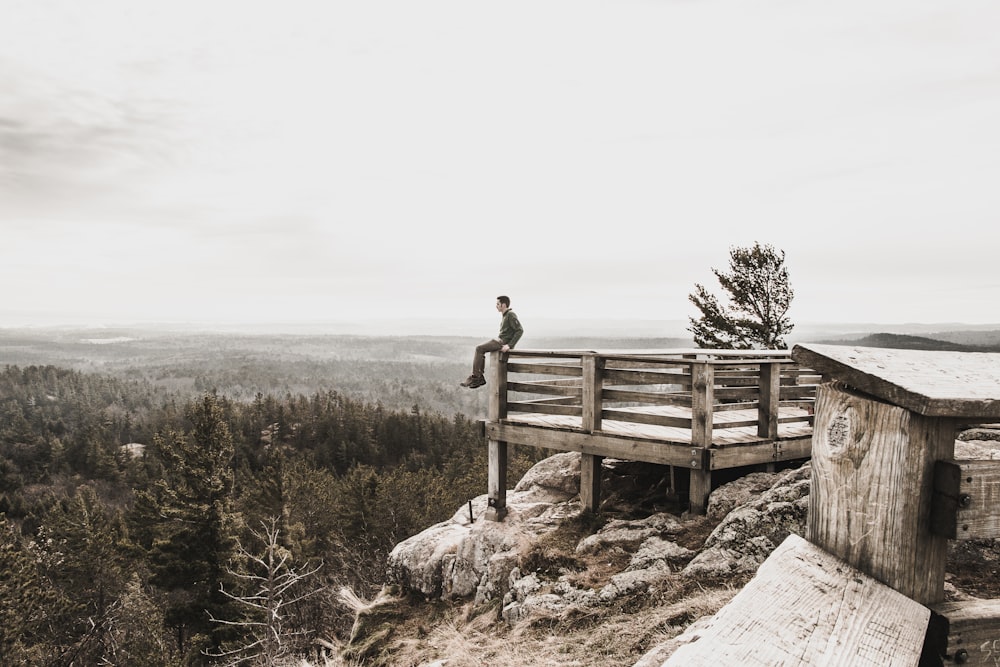 person sitting on brown wooden railings surrounded by trees