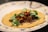 A corn tortilla topped with shredded meat, fresh cilantro leaves, and a red chili pepper. The tortilla is placed on a decorative plate with blue floral designs around the edge.