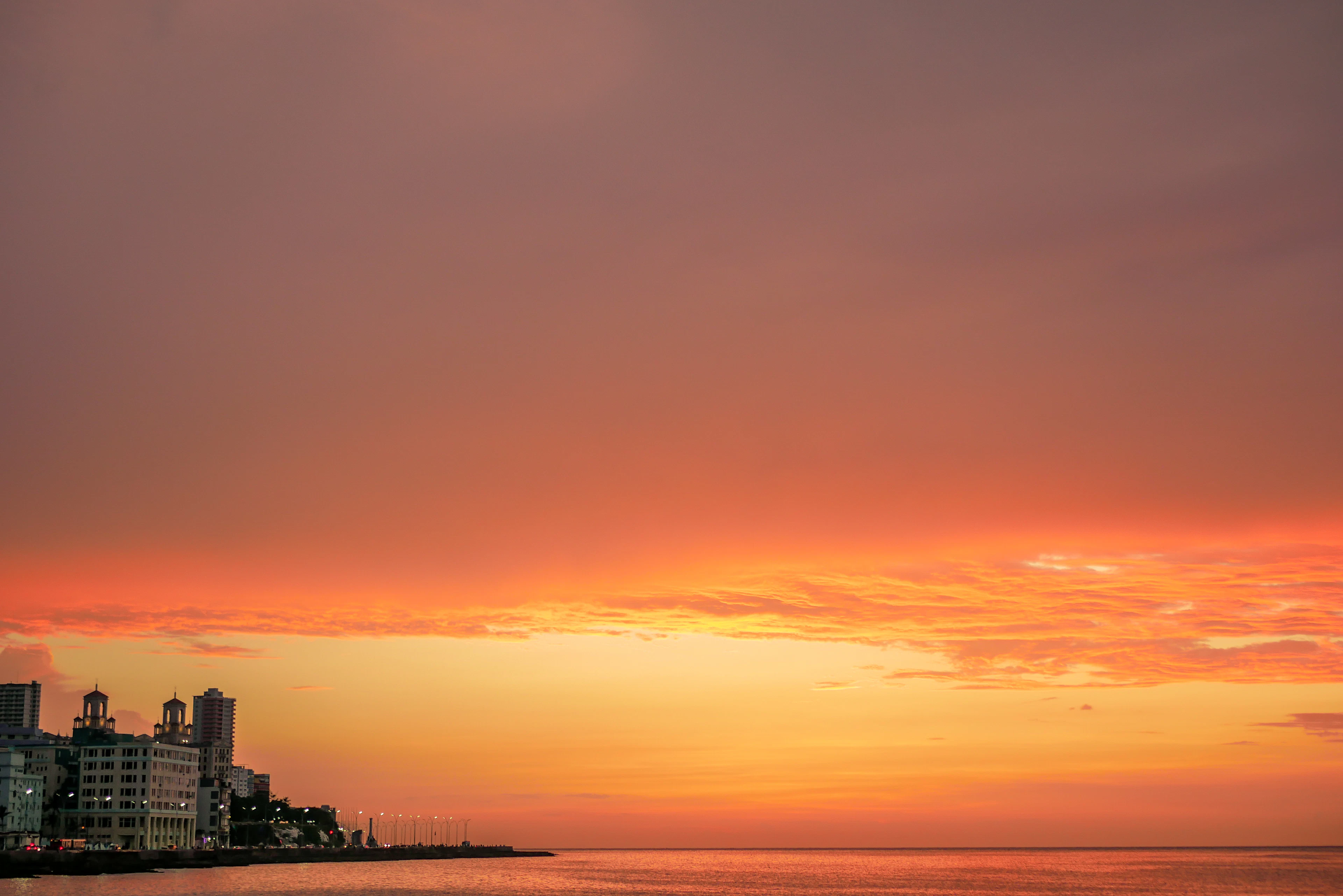 An orange sunset over the sea, with buildings silhouetted along Havana's Malecón