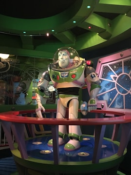 A large, detailed statue of a space-themed animated character stands in an indoor setting. The statue is placed within a circular display surrounded by sci-fi and space-themed decorations. The character is dressed in a space suit featuring green, white, and purple colors, with a clear helmet covering the head.