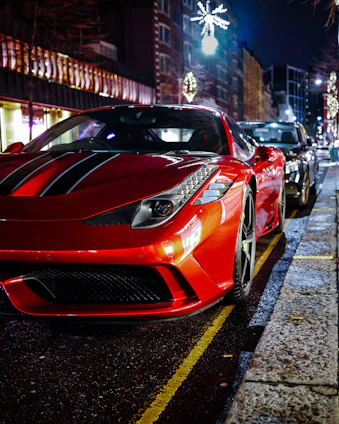 A sleek crimson luxury car parked on a city street at dusk, with soft urban lights reflecting off its polished surface.