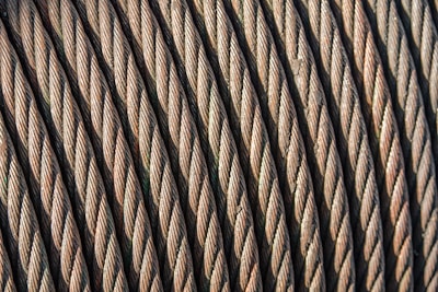 Close-up view of coiled steel cables arranged in parallel, showcasing the intricate twisting and texture of the metal strands. The image highlights the durability and strength of the cables.