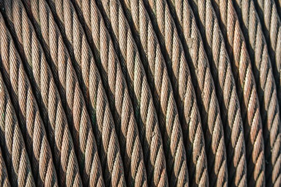 Close-up view of coiled steel cables arranged in parallel, showcasing the intricate twisting and texture of the metal strands. The image highlights the durability and strength of the cables.