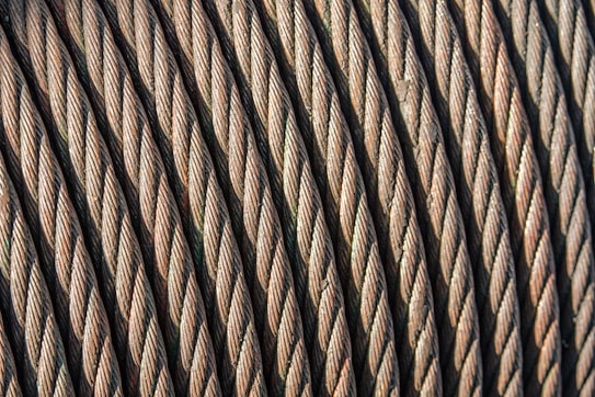 Close-up view of coiled steel cables arranged in parallel, showcasing the intricate twisting and texture of the metal strands. The image highlights the durability and strength of the cables.