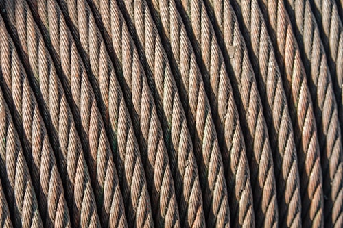 Close-up view of coiled steel cables arranged in parallel, showcasing the intricate twisting and texture of the metal strands. The image highlights the durability and strength of the cables.