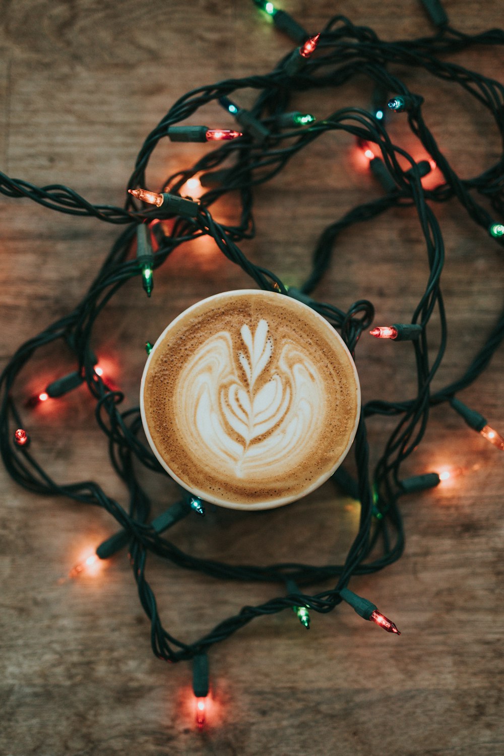 Tasse Cappuccino und eingeschaltete Lichterkette auf brauner Holzoberfläche